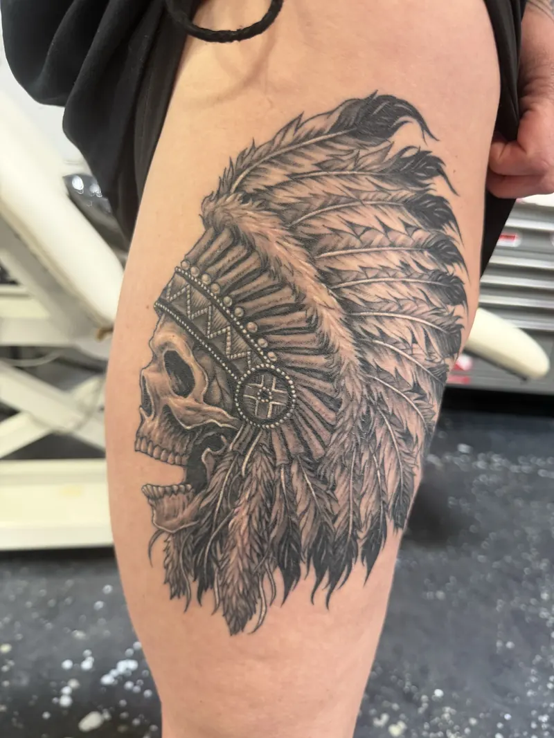 Black and grey skull in a feathered headdress tattoo by Moose, Calgary Tattoo Company